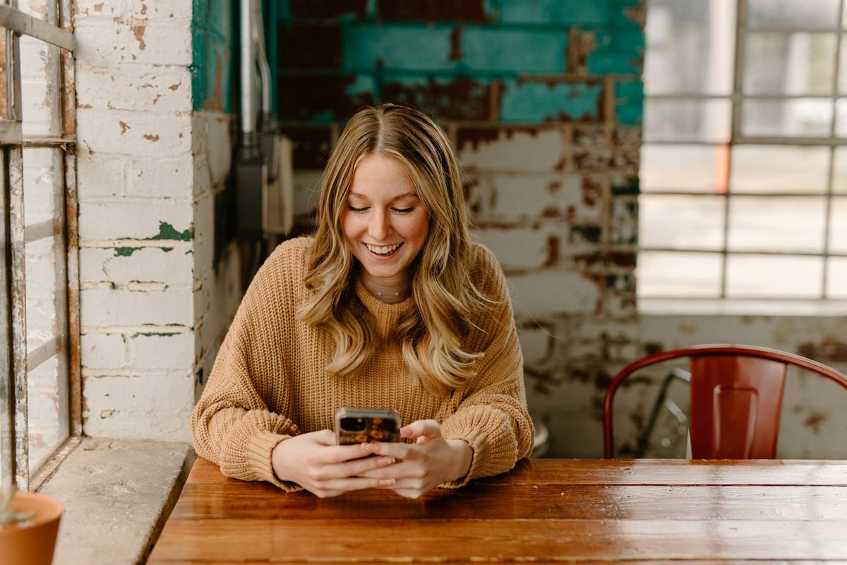 A woman smiling at her phone at a cafe table