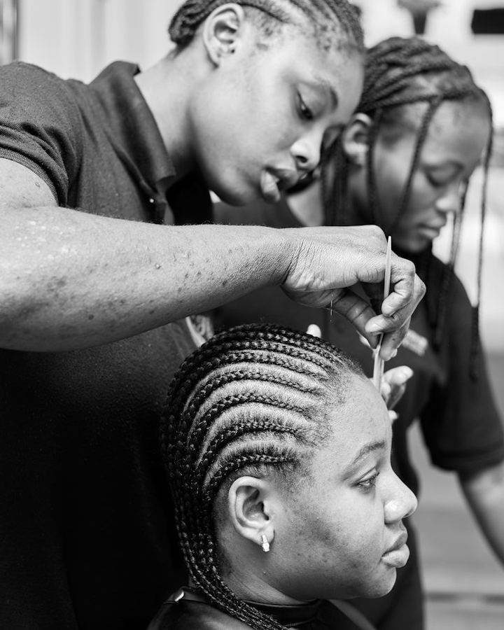 Two stylists braiding a client's hair